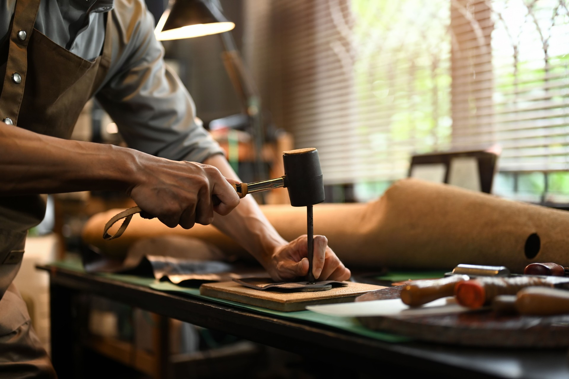 Male artisan using a hammer and other tools to shape and detail the leather piece in the workshop